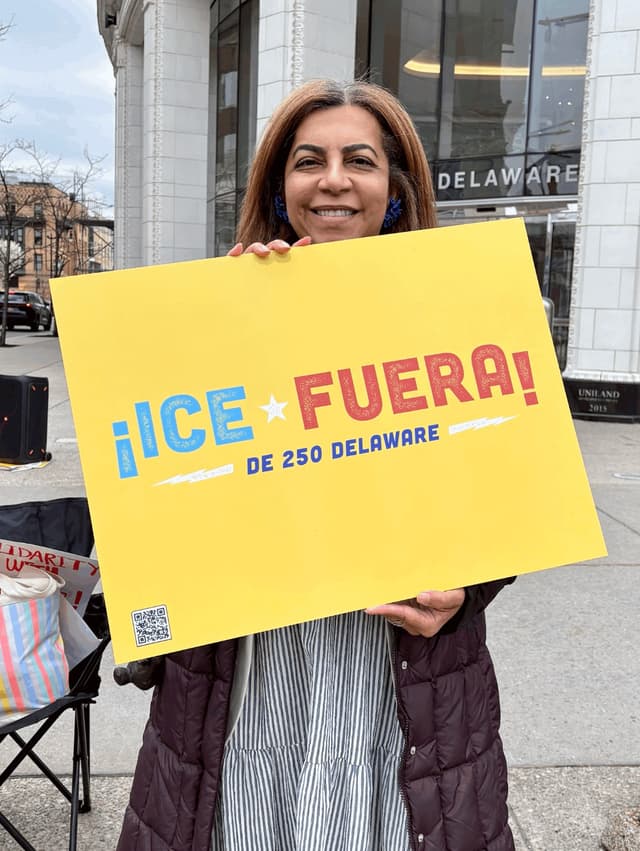 Supporter holding a yellow '¡ICE Fuera! de 250 Delaware' sign